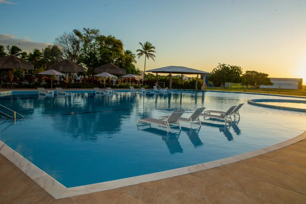 Piscina ao entardecer com espreguiçadeiras e quiosques de palha