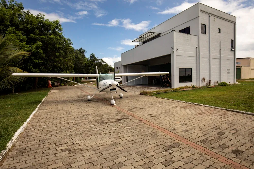 Avião monomotor branco em frente ao hangar