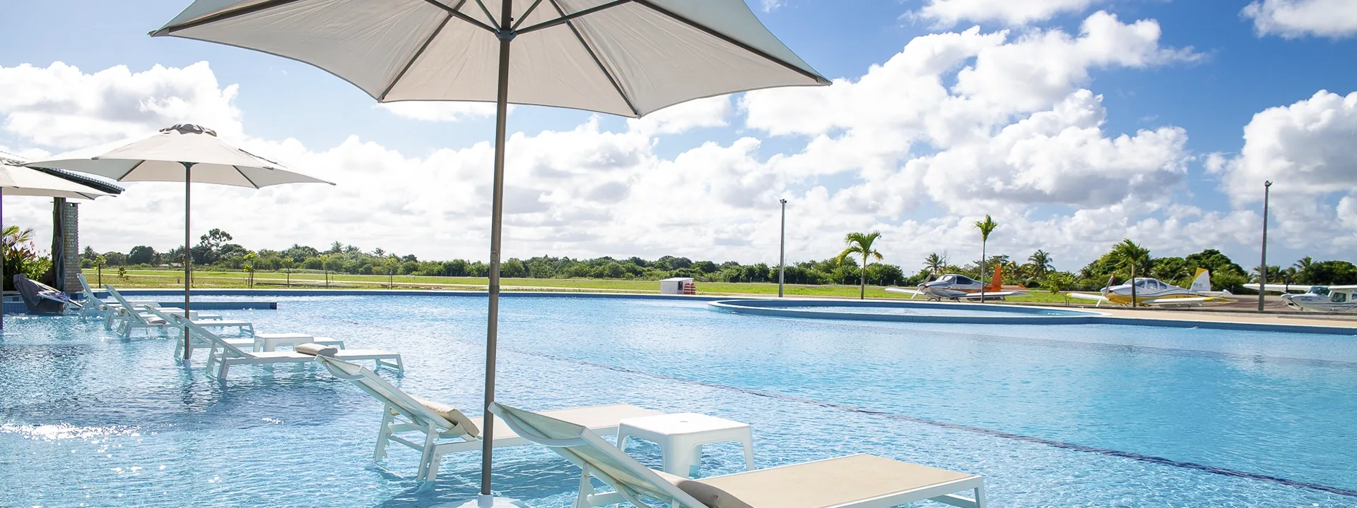 Piscina com espreguiçadeiras e aviões estacionados ao fundo